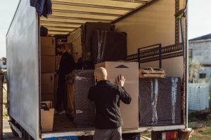 Deux professionnels d’entreprises de débarras chargent des cartons et du mobilier emballé dans un camion de déménagement ouvert en extérieur