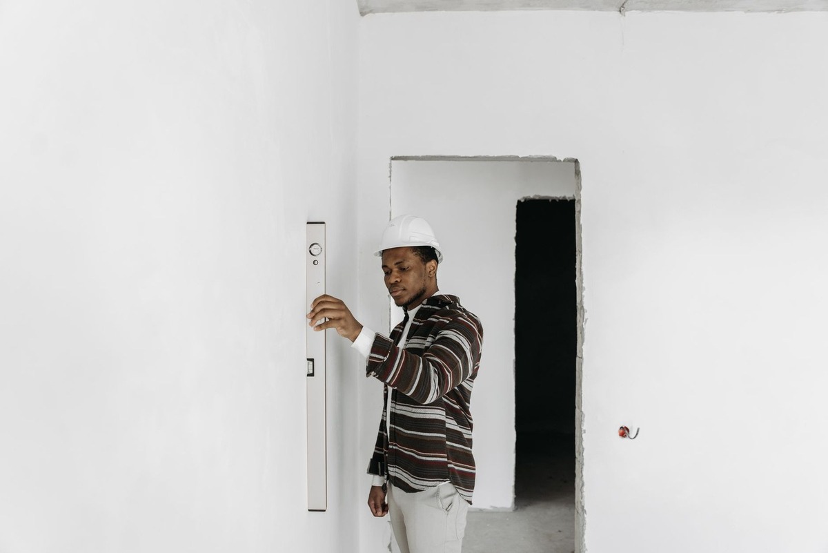 Homme en blouson rayé utilisant un niveau à bulle sur un mur blanc