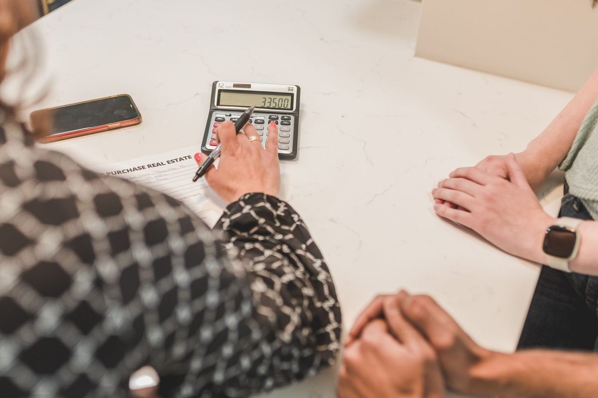 Une personne écrit sur un papier avec une calculatrice et un téléphone à proximité