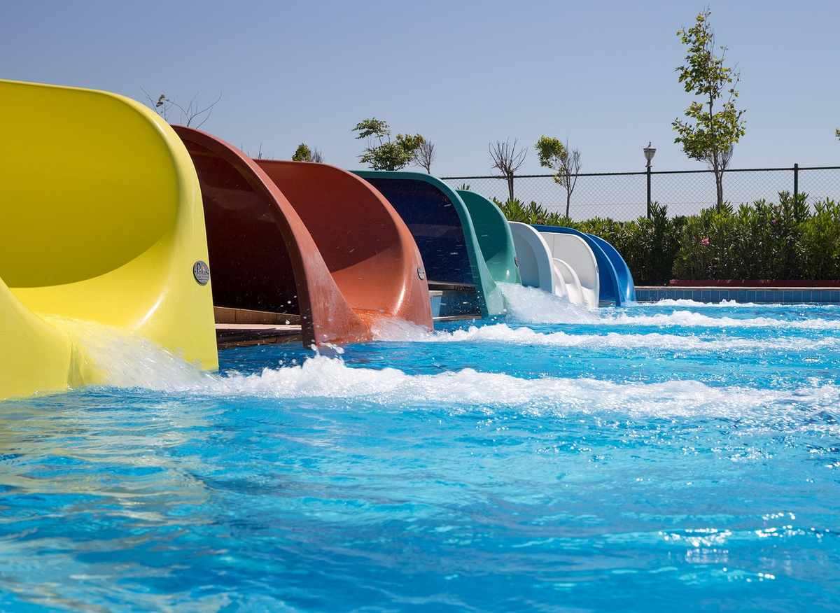 Glissades aquatiques colorées dans une piscine, avec végétation et clôture en arrière-plan Glissades aquatiques colorées dans une piscine, avec végétation et clôture en arrière-plan
